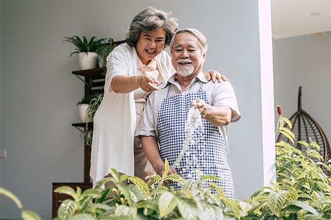 A couple standing in front of a house watering a plant.